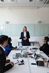 Female colleague interacting to businesswoman standing by conference table during meeting with coworkers - MASF13533