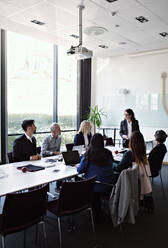 Businesswoman interacting to female colleague sitting with coworkers at conference table during meeting in board room - MASF13534