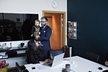 Smiling businesswoman looking male colleague with son standing in office - MASF13556