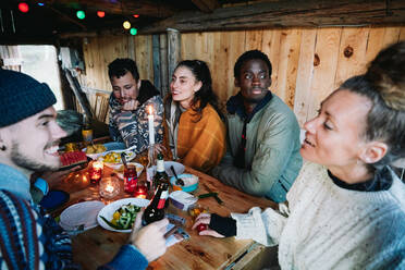 Male and female friends talking while having food on table in log cabin - MASF13578
