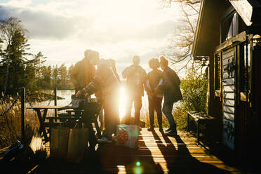 Silhouette Freunde im Gespräch, während außerhalb Hütte vor dem See bei Sonnenuntergang stehen - MASF13594