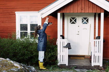 Seitenansicht einer jungen Frau, die ihre Schuhe vor einem Haus trocknet - MASF13601
