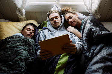 Hohe Winkel Ansicht von Freunden beobachten Film über digitale Tablet, während auf dem Bett in der Hütte liegen - MASF13608