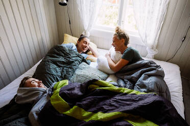 Hoher Blickwinkel auf fröhliche männliche und weibliche Freunde, die sich auf dem Bett liegend in einem Ferienhaus unterhalten - MASF13610