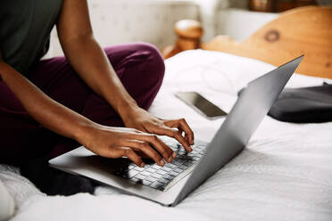 Low section of young woman using laptop while sitting on bed at home - MASF13629