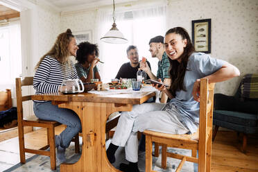 Portrait of smiling young woman using smart phone while sitting with friends at home - MASF13654