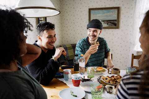 Cheerful friends talking while enjoying food in social gathering at home stock photo