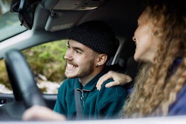 Junge Frau im Gespräch mit lächelndem männlichen Freund beim Autofahren - MASF13670