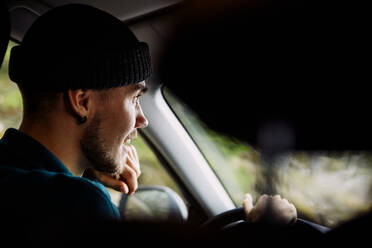 Smiling young man wearing knit hat while driving car - MASF13676