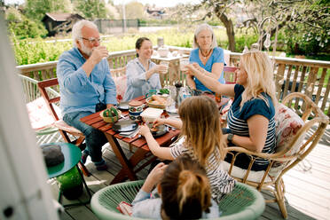 Multi-generational family toasting glasses while sitting at table in patio - MASF13686