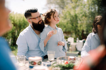 Girl having food with parents at table in patio - MASF13689