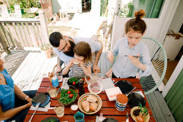 High angle view of girl using mobile phone while having food with family at home - MASF13691