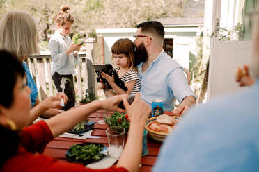 Mehrgenerationenfamilie beim Essen, während die Töchter im Innenhof die Technik nutzen - MASF13693