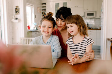 Mutter und Töchter schauen auf den Laptop, während sie im Wohnzimmer sitzen - MASF13695