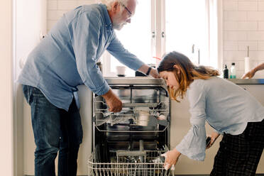 Grandfather assisting granddaughter in cleaning dishwasher at kitchen - MASF13700