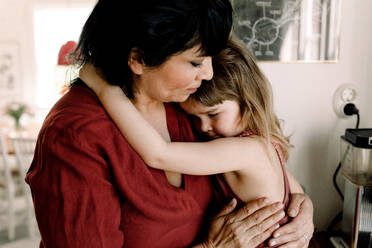 Besorgte Mutter hält ihre traurige Tochter im Arm, während sie zu Hause steht - MASF13704