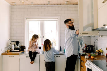 Mädchen schaut auf die arbeitende Schwester, während der Vater in der Küche Hausarbeiten erledigt - MASF13707