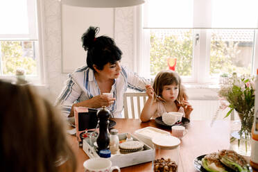 Mutter sieht ihre Tochter beim Frühstück am Esstisch an - MASF13712