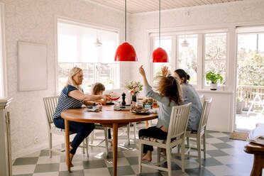 Mütter frühstücken mit ihren Töchtern, während sie am Esstisch im Haus sitzen - MASF13713