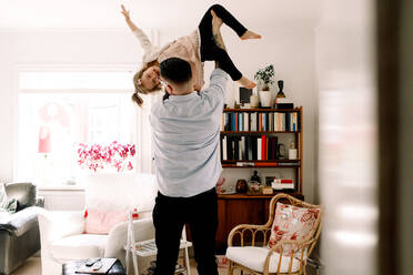 Rear view of playful father lifting cheerful daughter in living room at home - MASF13718