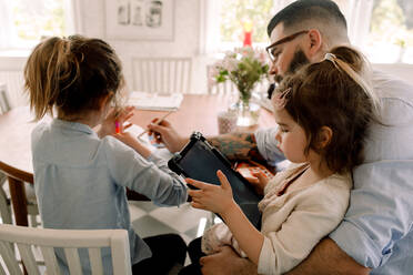 Mädchen, das ein digitales Tablet benutzt, während der Vater seiner Tochter am Esstisch bei den Hausaufgaben hilft - MASF13720