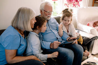 Großeltern und Enkelkinder nutzen ein digitales Tablet, während sie zu Hause im Wohnzimmer sitzen - MASF13731
