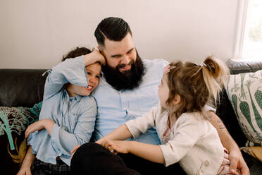 Glücklicher Vater spielt mit fröhlichen Töchtern, während er zu Hause auf dem Sofa sitzt - MASF13732
