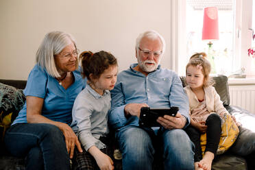 Grandparents sitting with grandchildren while using digital tablet in living room at home - MASF13734