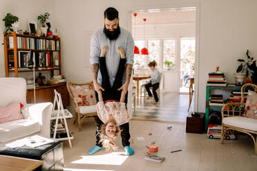 Playful father swinging girl while standing in living room at home - MASF13735