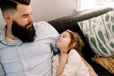 Hoher Blickwinkel des Vaters, der seine Tochter anschaut, während er sich zu Hause auf dem Sofa ausruht - MASF13736