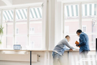 Männliche Computerprogrammierer diskutieren am Schreibtisch am Fenster im Büro - MASF13765