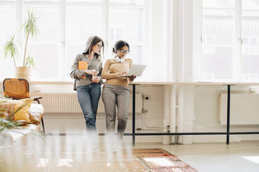 Weibliche Programmierer, die einen Laptop benutzen, während sie am Fenster im Büro stehen - MASF13767