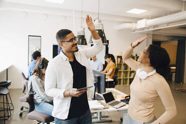 Lächelnde Programmierer geben sich High-Five, während sie mit Kollegen im Hintergrund arbeiten - MASF13779