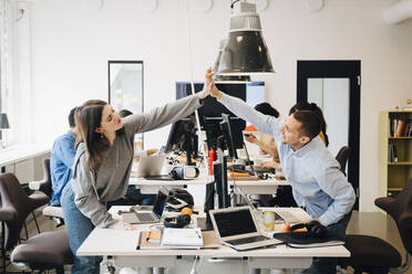 Glückliche männliche und weibliche Computerprogrammierer machen High-Five über Computer am Schreibtisch in kreativen Büro - MASF13780