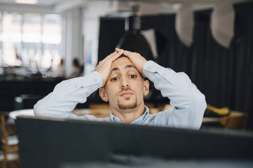 Exhausted computer programmer with head in hands looking at computer while working in office - MASF13792