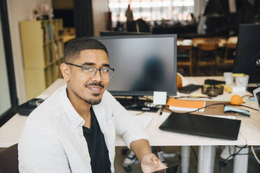 Portrait of confident computer hacker sitting at desk in office - MASF13799