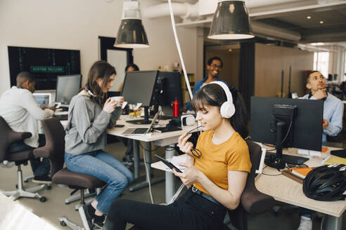 Eine IT-Fachfrau benutzt ein digitales Tablet, während ihre Kollegen im Hintergrund im Kreativbüro arbeiten - MASF13833
