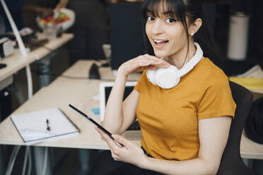 Porträt einer glücklichen Computer-Hackerin, die im Büro sitzend ein digitales Tablet benutzt - MASF13834