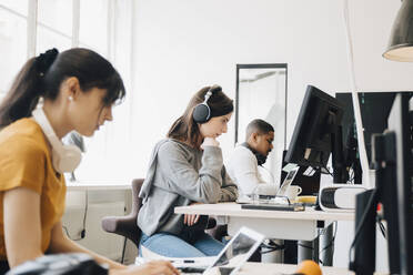 Seitenansicht von konzentrierten Programmierern, die Laptops auf dem Schreibtisch benutzen, während sie im Büro sitzen - MASF13835