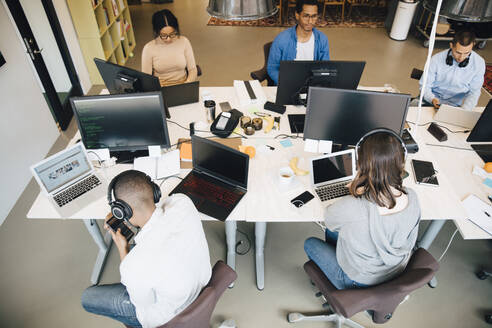 Hochformatige Ansicht von IT-Fachleuten, die an einem Schreibtisch in einem kreativen Büro sitzen und Technologie verwenden - MASF13838