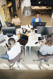 Blick von oben auf männliche und weibliche Programmierer, die im Büro sitzend Technik auf dem Schreibtisch benutzen - MASF13839