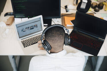 Rückansicht eines männlichen IT-Fachmanns, der einen Laptop auf dem Schreibtisch benutzt, während er in einem kreativen Büro sitzt - MASF13840