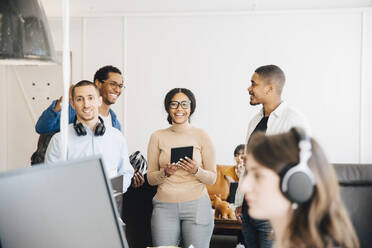 Lächelnde IT-Ingenieure im Gespräch, während sie in einem kreativen Büro an der Wand stehen - MASF13843