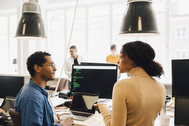 Computer hackers discussing at desk while sitting in creative office - MASF13857