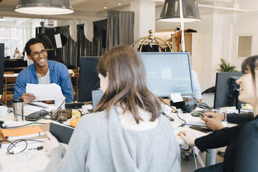 Fröhliche männliche und weibliche IT-Fachleute, die sich am Schreibtisch in einem kreativen Büro unterhalten - MASF13865