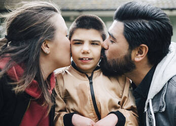 Seitenansicht der Eltern, die ihren autistischen Sohn im Hof küssen - MASF13874