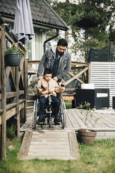 Father pushing autistic son sitting on wheelchair in yard - MASF13876