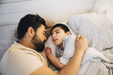 High angle view of father with disable son lying on bed at home - MASF13885