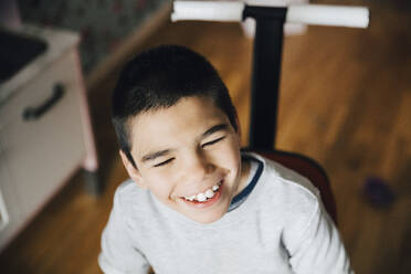 Blick von oben auf einen glücklichen behinderten Jungen, der wegschaut, während er zu Hause im Rollstuhl sitzt - MASF13889