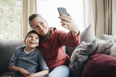 Lächelnde Mutter, die ein Selfie mit ihrem autistischen Sohn macht, während sie zu Hause auf dem Sofa sitzt - MASF13910